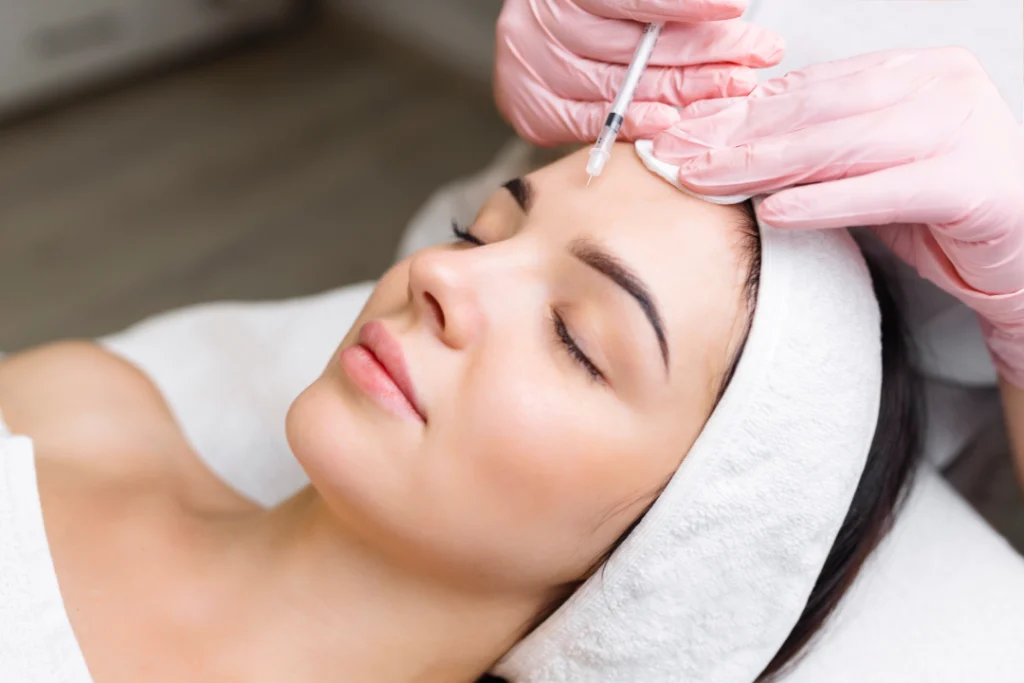 A woman receiving Botox injections on her forehead while lying on a treatment bed.