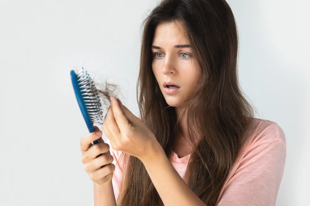 Woman concerned about hair loss holding a hairbrush with hair.